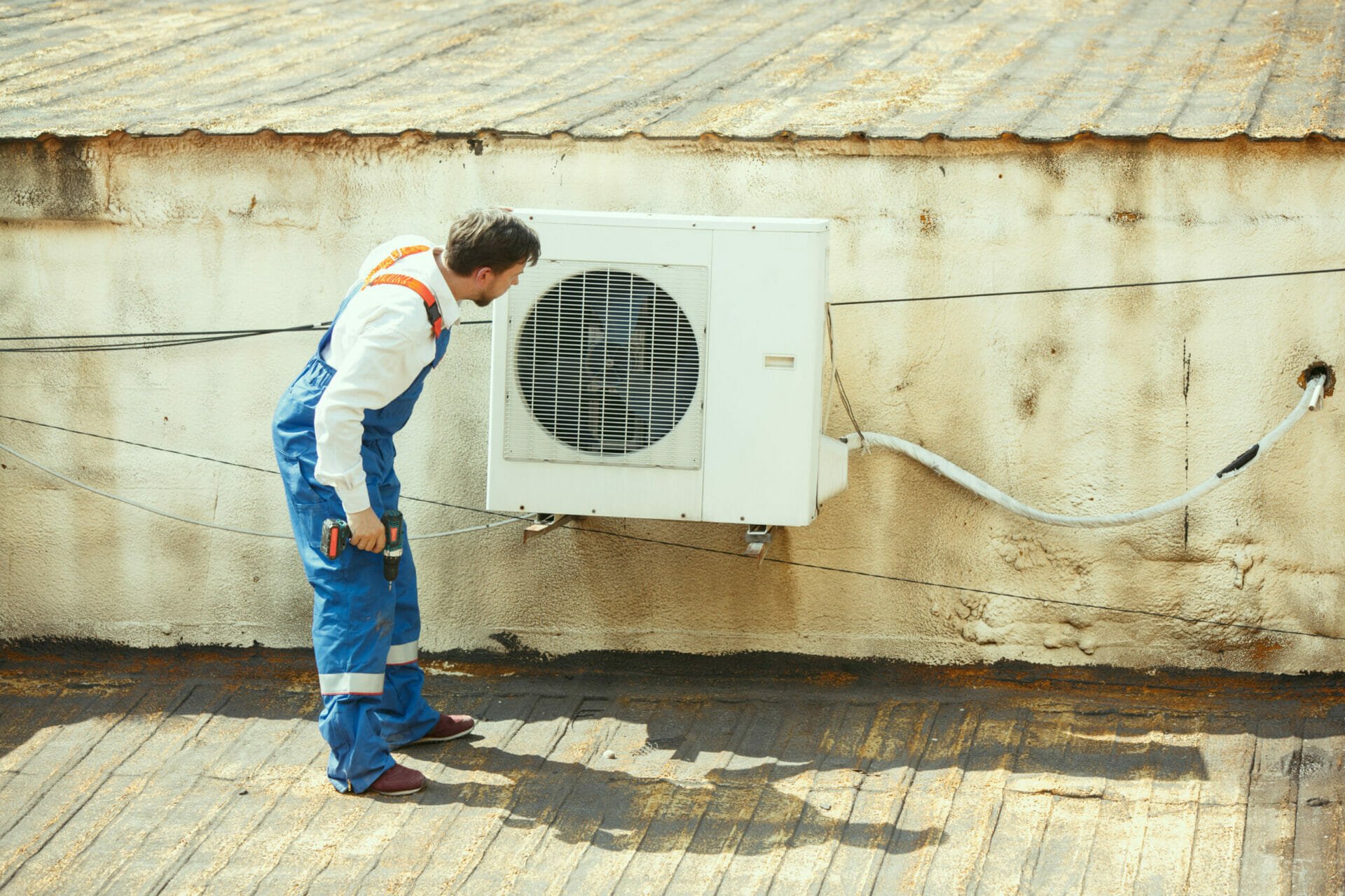 A man in overalls fixing an air conditioner for 24/7 air conditioning repair in Austin.