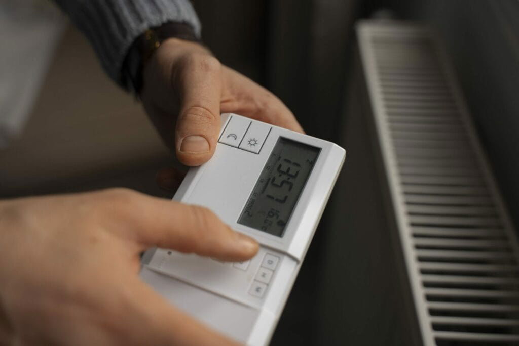 A person adjusts the temperature on a digital thermostat mounted near a radiator, showcasing the efficiency of appliances expertly serviced by Patriot Appliance Repair & HVAC in Austin.