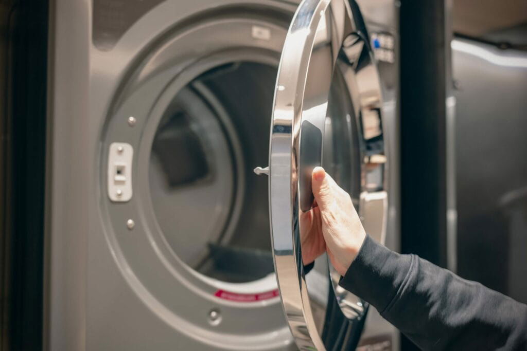 A hand opening the door of a front-loading washing machine, showcasing high-quality appliances from Patriot Appliance Repair & HVAC in Austin.